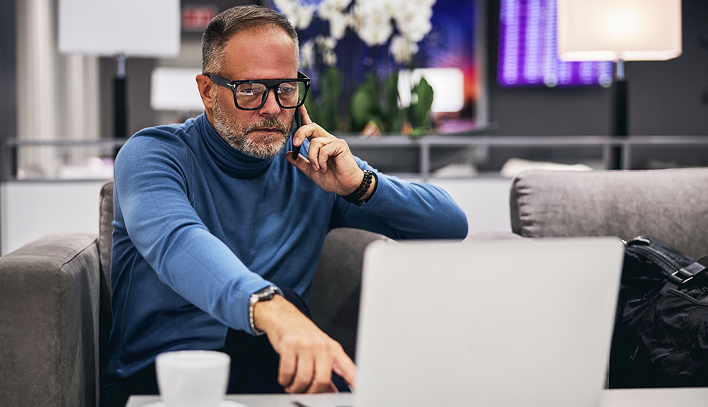 Man on a phone call pointing to his laptop and looking dissatisfied